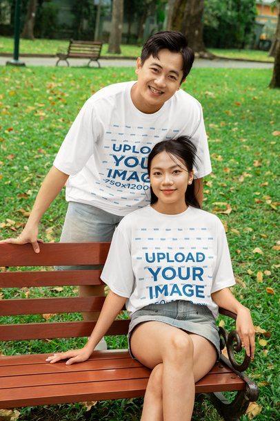 Mockup of a Happy Couple Wearing Oversized T-Shirts and Posing in a Park Bench