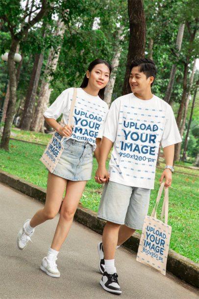 Mockup of a Happy Man and a Woman Wearing T-Shirts While Walking in the Park With Sublimated Tote Bags