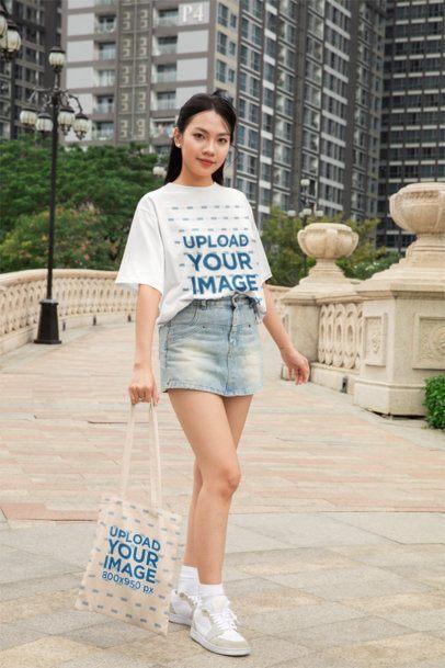 Oversized Tee Mockup of a Smiling Woman Posing With a Tote Bag in a City Bridge