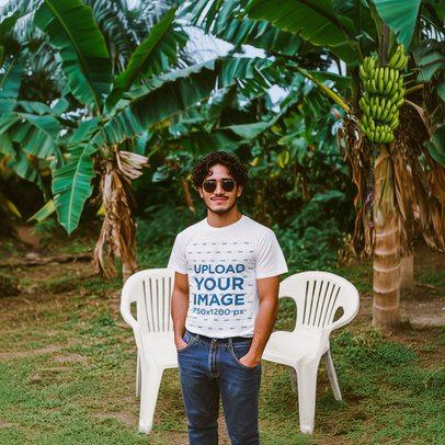 T-Shirt Mockup Featuring a Man Standing in Front of Two Plastic Chairs and Banana Plants