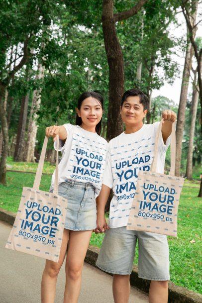 Tote Bag Mockup of a Happy Couple Wearing Oversized T-Shirts in the Park